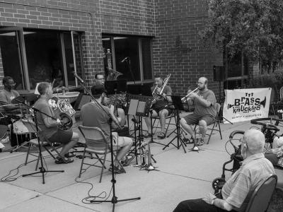 A black and white photo of the five members of The Brass Knuckles performing outdoors