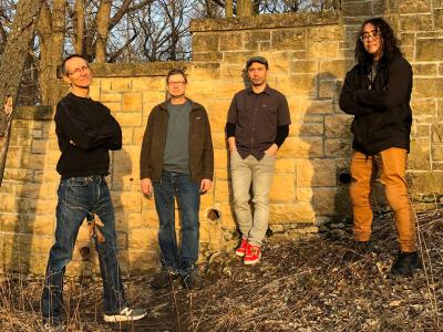 The four members of the band Inside Pocket, standing in front of a stone wall at sunset.