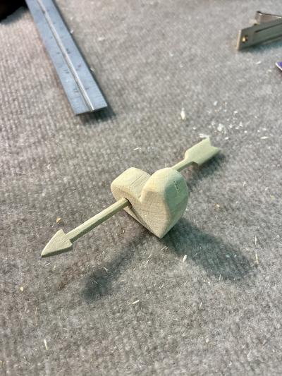 Image of a charm made of wood with an arrow going through a heart.