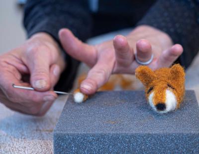 hands using a needle to felt an orange and white fox head and tail