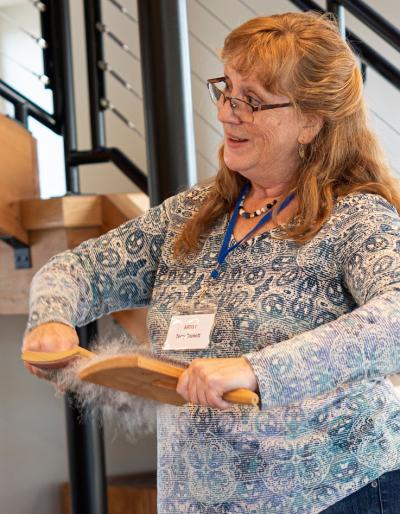 A woman in contemporary clothing hand-carding wool