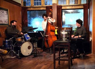 The Lance Lettelier Trio, with one member playing a drum set, one playing bass, and the third playing keyboard.