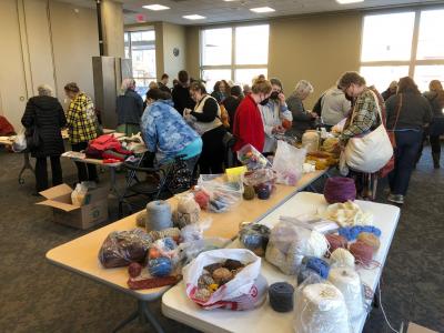 A photo of fiber arts materials and people browsing through them in the Sequoya community room