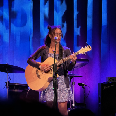 A photo of carisa playing acoustic guitar on a stage